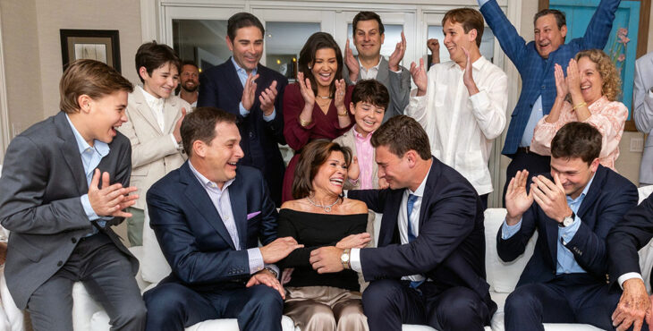 The Mendoza family gathered in a living room during a televised sports draft event, seated and standing around a couch with hands raised or clapping.